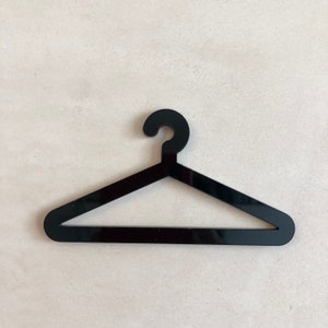 May include: A black, minimalist clothing hanger. The hanger is made of a solid, glossy material and has a simple, modern design. The hook is curved, and the body of the hanger is a triangle shape.