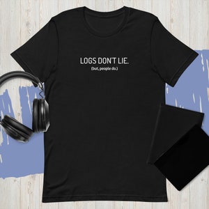 Może przedstawiać: Czarny t-shirt z białym napisem "LOGS DON'T LIE. (but, people do.)". Koszulka jest prezentowana z czarnymi słuchawkami i dwoma czarnymi notatnikami.