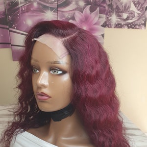 May include: A long, wavy burgundy wig with a lace front. The wig is styled in loose waves and has a natural-looking hairline.
