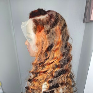 May include: A long, wavy, brown and orange wig with a lace front. The wig is styled in loose curls.