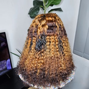 May include: A long, curly wig with a dark brown base and blonde highlights. The wig is styled in loose waves and appears to be made of human hair.