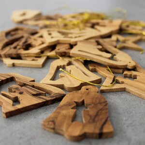 May include: A pile of wooden Christmas decorations in the shape of bells, stars, and angels. The decorations are made from olive wood and have a natural wood finish.