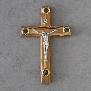 Pode incluir: Crucifixo de madeira com uma figura prateada de Jesus Cristo. A cruz é feita de madeira castanha clara com detalhes dourados e incrustações circulares. A figura de Cristo é prateada, com os braços estendidos.
