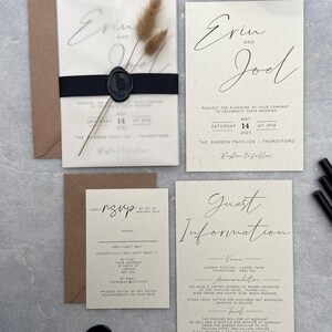 May include: Wedding invitation suite featuring a translucent invitation with the names "Erin and Joel" in elegant script, a black ribbon, and a wax seal. Includes RSVP and guest information cards, all in a neutral color palette. Dried floral accents add a natural touch.