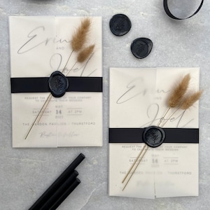 May include: Elegant wedding invitations with a minimalist design. Each invitation features a translucent overlay, black ribbon, and a black wax seal with a botanical design. Dried flowers and black sealing wax sticks complete the aesthetic.