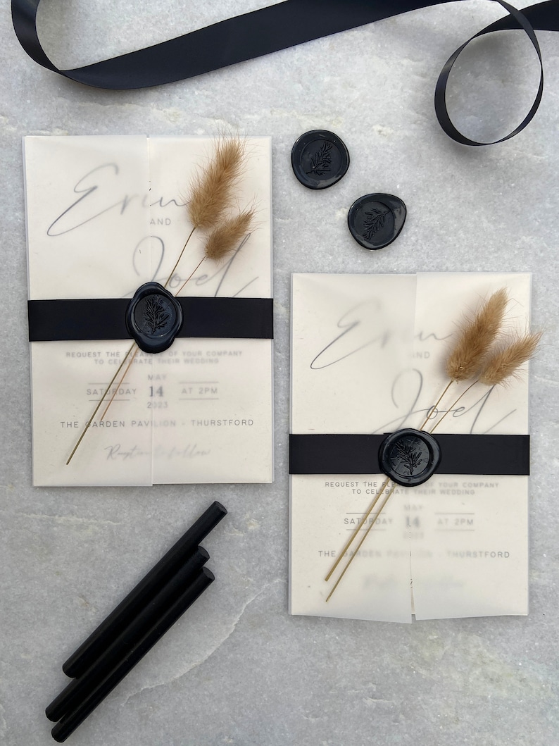 May include: Elegant wedding invitations with a minimalist design. Each invitation features a translucent overlay, black ribbon, and a black wax seal with a botanical design. Dried flowers and black sealing wax sticks complete the aesthetic.
