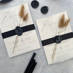 May include: Two wedding invitations with black ribbon, dried flowers, and black wax seals. The invitations have the names "Erin and Joel" and event details. Additional black wax sticks and ribbon are also visible.