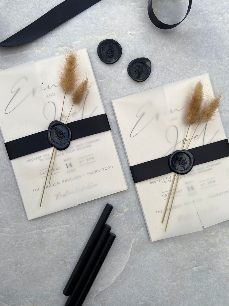 May include: Two wedding invitations with black ribbon, dried flowers, and black wax seals. The invitations have the names "Erin and Joel" and event details. Additional black wax sticks and ribbon are also visible.