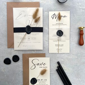 May include: Wedding stationery set featuring a Save the Date card, invitation, and menu. The cards are cream-colored with black text and sealed with black wax. Dried bunny tails and a black ribbon add decorative elements.