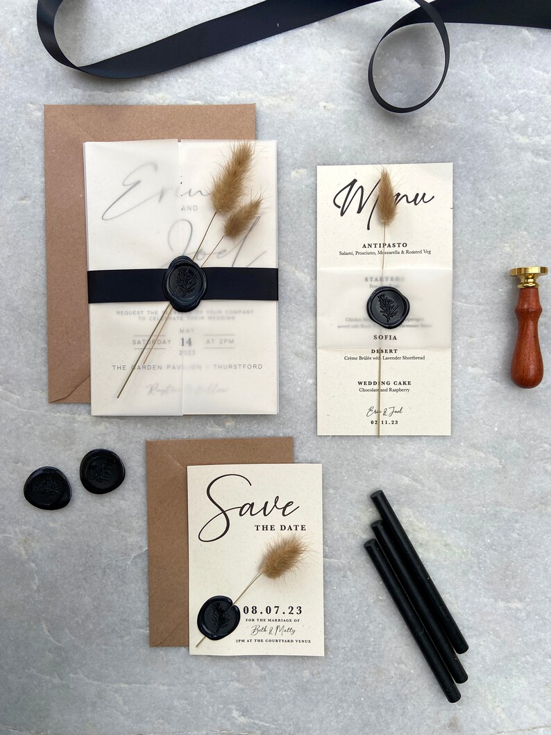 May include: Wedding stationery set featuring a Save the Date card, invitation, and menu. The cards are cream-colored with black text and sealed with black wax. Dried bunny tails and a black ribbon add decorative elements.