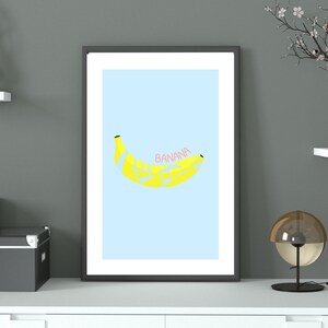 May include: A framed print of a yellow banana on a light blue background with the word "banana" written in pink letters.