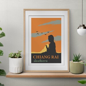 K&ouml;nnte beinhalten: Ein Vintage-Reiseposter mit orangefarbenem Hintergrund und einer Silhouette einer Person, die auf einem Berg sitzt. Das Poster zeigt den Text "CHIANG RAI" und "เชียงราย" in Thai.