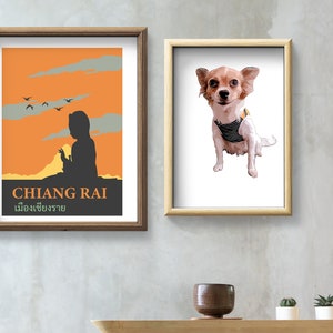 K&ouml;nnte beinhalten: Zwei gerahmte Drucke an einer grauen Wand. Der Druck links ist ein Vintage-Reiseposter f&uuml;r Chiang Rai, Thailand. Der Druck rechts ist eine Cartoon-Illustration eines kleinen Hundes, der eine gestreifte Weste tr&auml;gt.