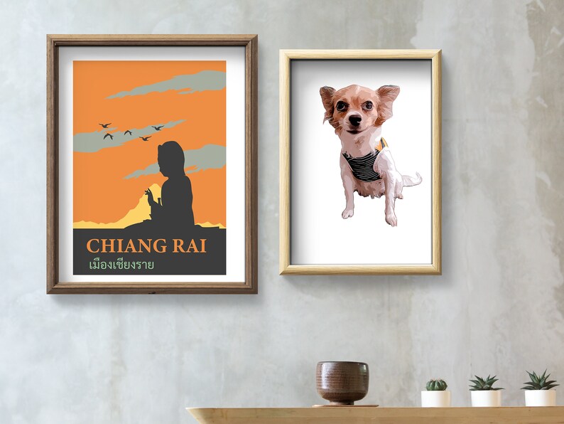 K&ouml;nnte beinhalten: Zwei gerahmte Drucke an einer grauen Wand. Der Druck links ist ein Vintage-Reiseposter f&uuml;r Chiang Rai, Thailand. Der Druck rechts ist eine Cartoon-Illustration eines kleinen Hundes, der eine gestreifte Weste tr&auml;gt.
