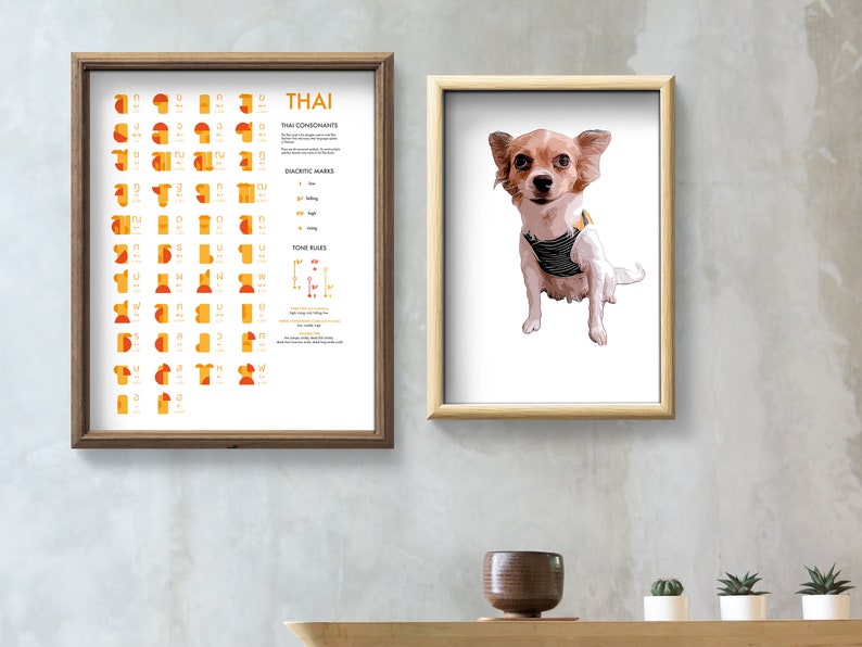 May include: Two framed prints on a light gray wall. The print on the left is a chart of the Thai alphabet with the title "THAI". The print on the right features a small, brown and white chihuahua wearing a striped vest.