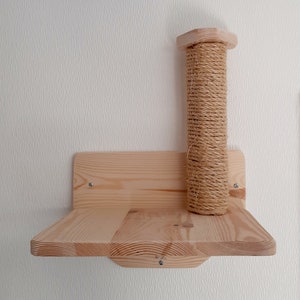 Peut inclure: Une étagère en bois pour chat avec un poteau à gratter recouvert de sisal. L'étagère est en bois naturel et a un design simple. L'étagère est fixée à un mur blanc.