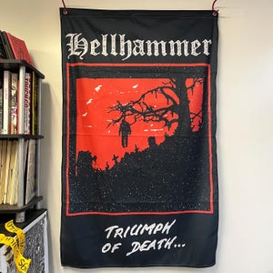 Może przedstawiać: Czarno-czerwona flaga z napisem "Hellhammer" i "Triumph of Death..." w kolorze białym. Flaga przedstawia sylwetkę drzewa z wiszącą postacią na czerwonym tle.