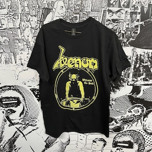 Op de afbeelding: Zwart T-shirt met een geel Venom-logo en een gele afbeelding van een demon met de tekst "Welcome to Hell".