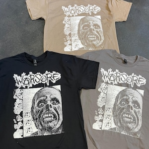 Puede incluir: Tres camisetas de manga corta en color beige, negro y gris. Cada camiseta presenta una impresión gráfica con la palabra "WARSORE" en una fuente distorsionada sobre una imagen detallada en escala de grises de una cara.