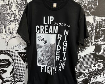 Könnte beinhalten: Schwarzes T-Shirt mit einem weißen Grafikdruck, der "Lip Cream Rider Night More Than Three Fight!" im Punkrock-Stil sagt. Die Grafik enthält auch eine Zeichnung einer Rakete.