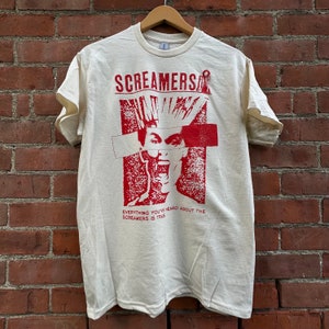 Könnte beinhalten: Ein weißes T-Shirt mit einem roten Grafikdruck einer Person mit einem Irokesenschnitt und dem Text "Screamers" und "Everything you've heard about the Screamers is true".