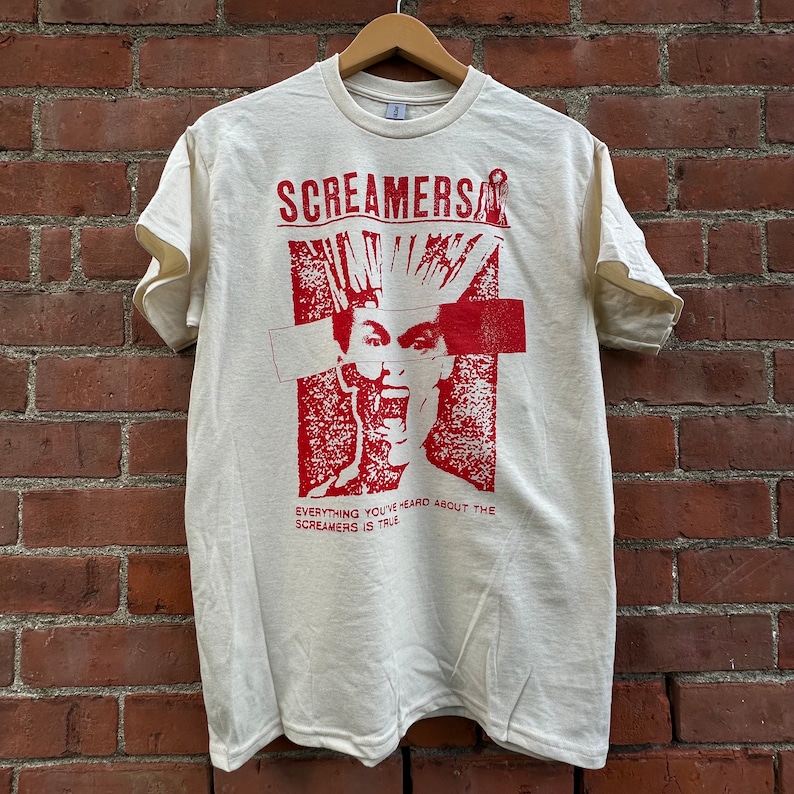 Puede incluir: Una camiseta blanca con un estampado gr&aacute;fico rojo de una persona con un mohawk y el texto "Screamers" y "Everything you've heard about the Screamers is true".