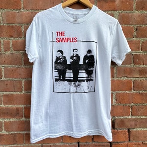May include: White t-shirt with a black and white image of a band called "THE SAMPLES". The band members are standing in front of a brick wall.