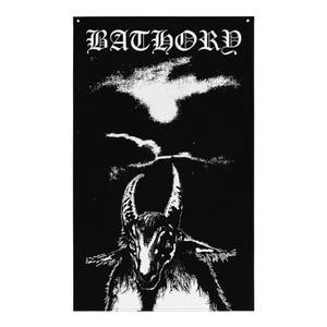 May include: A rectangular black wall flag featuring the white text BATHORY at the top in a gothic font. Below the text is a high-contrast white graphic illustration of a horned goat head centered against a solid black background.