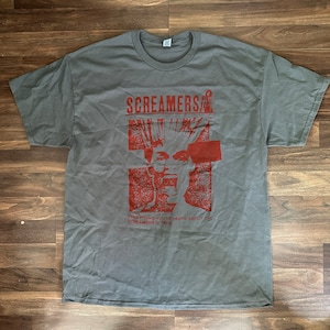 Puede incluir: Camiseta gris con un estampado gr&aacute;fico rojo de una persona con el pelo de punta y el texto "Screamers" y "Everything you've heard about the Screamers is true".