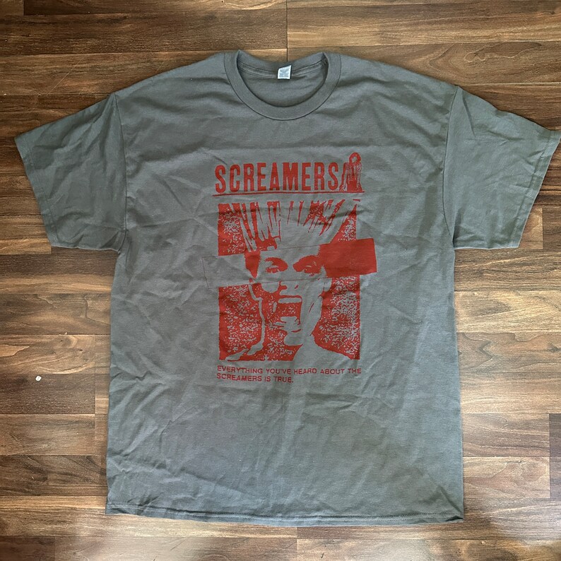 Puede incluir: Camiseta gris con un estampado gr&aacute;fico rojo de una persona con el pelo de punta y el texto "Screamers" y "Everything you've heard about the Screamers is true".