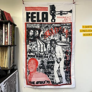 Könnte beinhalten: Ein weißer Stoffposter mit einem schwarzen und roten Design, das ein Porträt von Fela Kuti, eine Trompete und den Text "FELA RANSOME KUTI AND HIS AFRICA 70" zeigt. Der Poster ist von einer Collage aus Bildern und Text umgeben.