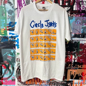Puede incluir: Camiseta blanca con un gráfico azul y blanco de la banda Circle Jerks. El gráfico presenta una serie de imágenes de una persona saltando en el aire.