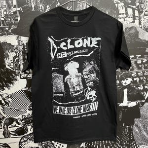 May include: Black t-shirt with a white graphic print of a band called "D-Clone" with the text "K17 NOT MUSIC!!!" and "WE MAKE DIS CLONE MUSIC!!!"  The graphic also includes the band's contact information: "contact: 090-1471-4923".