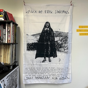 Op de afbeelding: Zwart-witte illustratie van een gekapte figuur die op een veld staat. De tekst "flix of PINK INGTANSA" staat bovenaan de afbeelding. De tekst "LYNNE NUCLEAT, d'ik diolch." staat onderaan de afbeelding.