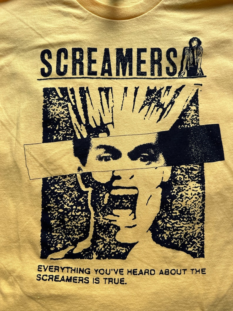 Puede incluir: Camiseta amarilla con un estampado gr&aacute;fico en blanco y negro de una persona gritando. El texto "Screamers" est&aacute; en la parte superior del gr&aacute;fico y el texto "Everything you've heard about the Screamers is true." est&aacute; en la parte inferior.