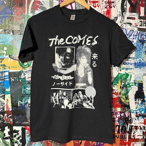 May include: Black t-shirt with a white graphic print of the band "The Comes". The graphic includes a photo of a woman with a microphone, the band's name, and the text "No Side" in Japanese and English.
