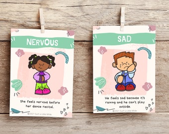 May include: Two illustrated cards with pink and green backgrounds. The first card shows a girl with brown skin and pigtails, wearing a purple shirt, green pants, and pink shoes. The text on the card reads "NERVOUS" and "She feels nervous before her dance recital." The second card shows a boy with brown hair, wearing a blue shirt, blue overalls, and red shoes. He is crying. The text on the card reads "SAD" and "He feels sad because it's raining and he can't play outside."