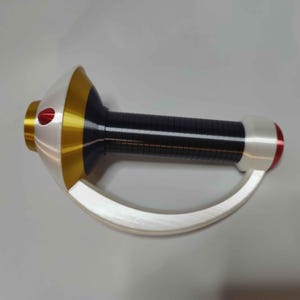 May include: A handheld prop featuring a black cylindrical grip with horizontal ridges, a gold and white flared base with a small red accent, and a curved white guard extending from the base to the pommel, which is capped with a red circular detail.