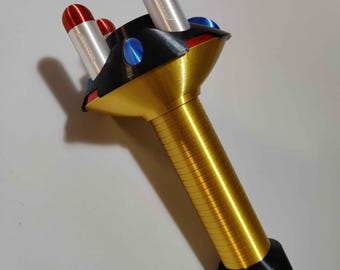 May include: A gold-coloured toy with a black base and three red and white rocket-shaped attachments. The toy has a black top with blue accents.