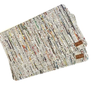 May include: Two rectangular placemats woven from thin, multicolored strips of paper or fabric, creating a textured, speckled appearance with dominant white, gray, and muted tones. Each mat features a small, rectangular brown leather-like tag.