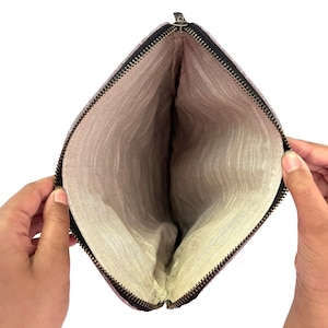 May include: Open, empty pouch with a black zipper and a light-colored interior. The pouch is held open, revealing the inside lining. The exterior fabric has a subtle, textured pattern.