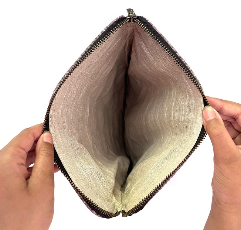 May include: Open, empty pouch with a black zipper and a light-colored interior. The pouch is held open, revealing the inside lining. The exterior fabric has a subtle, textured pattern.