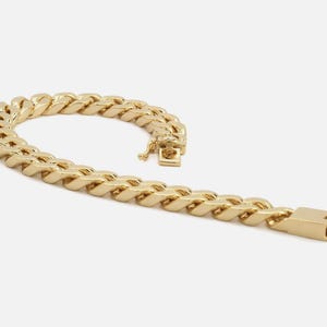 May include: A gold-colored chain bracelet with a curb link design. The bracelet is made of a shiny, metallic material and features a secure clasp. The links are thick and closely connected, creating a bold, eye-catching accessory.