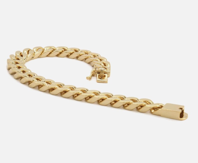 May include: A gold-colored chain bracelet with a curb link design. The bracelet is made of a shiny, metallic material and features a secure clasp. The links are thick and closely connected, creating a bold, eye-catching accessory.