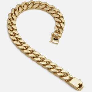 May include: A gold-colored curb chain bracelet with a secure clasp. The bracelet is made of interlocking oval links, creating a bold and classic design. The clasp is rectangular and features a secure closure mechanism.