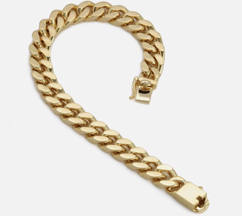 May include: A gold-colored curb chain bracelet with a secure clasp. The bracelet is made of interlocking oval links, creating a bold and classic design. The clasp is rectangular and features a secure closure mechanism.