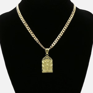 Pode incluir: Um colar dourado com um pingente que retrata uma figura religiosa. O pingente é retangular com um topo arqueado e um relevo detalhado. A corrente é do estilo elo de corrente grosso, apresentado sobre um fundo preto.