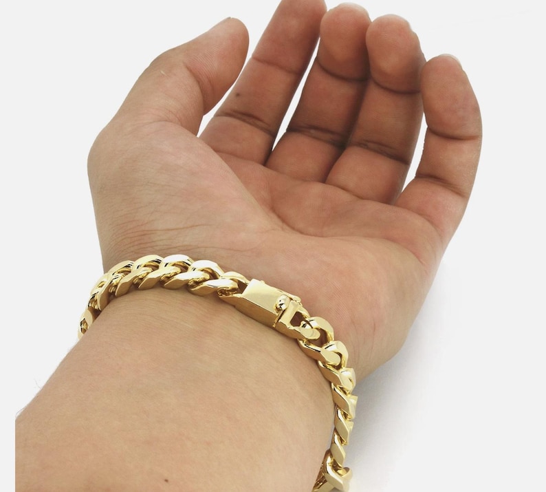 May include: A gold-colored curb chain bracelet. The bracelet is made of interlocking links and features a secure clasp. The jewelry is worn on the wrist and is displayed against a light background.