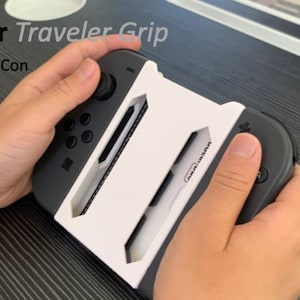 May include: A white and black Nintendo Switch Joy-Con controller grip with the text "CardGear Traveler Grip" printed on it. The grip is designed to hold two Joy-Con controllers together for a more comfortable gaming experience.