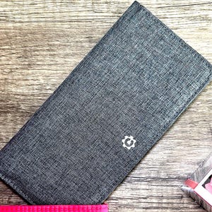 Cartera plegable de lona larga, delgada, gris, con bloqueo RFID y ventana para identificación. Capacidad para hasta 12 tarjetas. Bolsillo trasero con cremallera para llaves y monedas. Sencilla y clásica.